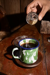 A man is making hot herbal tea in a traditional cup on a wooden table on a black background. Images from everyday life.
