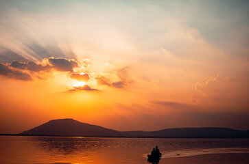 A beautiful golden sunset on the lake. Locals ride in a boat on a lake during a beautiful sunset. Sunset or sunrise landscape, panorama of beautiful nature.