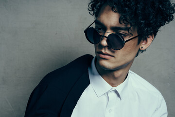 portrait of a curly-haired guy in a shirt with a jacket on his shoulder and glasses on his face close-up 