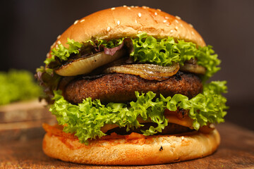 Hamburger with double vegan pea patty, caramelized onions and lettuce on mango wood board on dark...