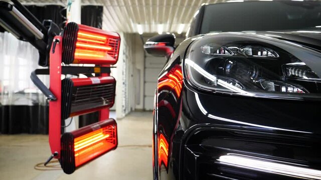 Infrared drying of car body parts after applying putty and paint on a white off-road vehicle in the body repair shop with red lanterns in the working environment. Concept of: Car Ceramic, Slow Motion.