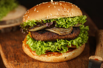 Hamburger with double vegan pea patty, caramelized onions and lettuce on mango wood board on dark wooden surface