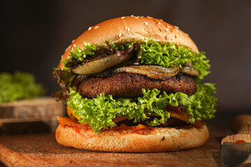 Hamburger with double vegan pea patty, caramelized onions and lettuce on mango wood board on dark wooden surface