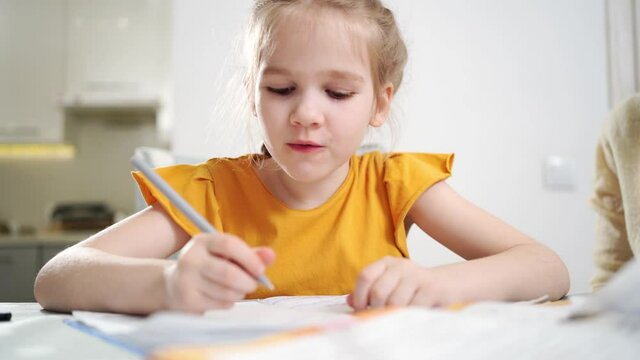 A schoolgirl does her homework and wipes the snot with your hand. complexities of correct and beautiful handwriting. family and distance learning. mom sits next to her