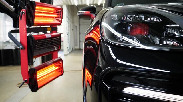 Infrared drying of car body parts after applying putty and paint on a white off-road vehicle in the body repair shop with red lanterns in the working environment. Concept of: Car Ceramic, Slow Motion.