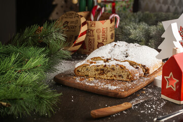 A traditional christmas pastry stollen with powdered sugar on a wooden board surrounded by festive decoration