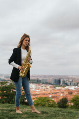 Naklejka premium Young blonde girl playing the saxophone in a park