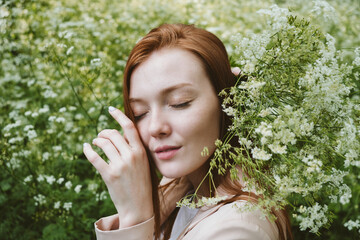 Mental Health Awareness Month, behavioral health care. Post COVID-19 pandemic mental health challenges. Red-haired young woman on green nature trees and flowers background