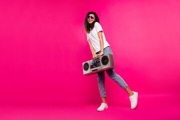 Full body photo of pretty millennial lady hold boom box wear spectacles t-shirt jeans sneakers isolated on pink background