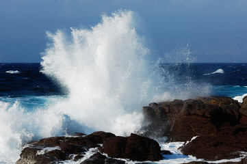 A large wave crashes into the rocks, forming white spray