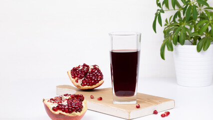 Banner. Fresh natural organic red pomegranate juice in a glass with pomegranate slices with seeds on a board, green flower in a pot, isolated white background.