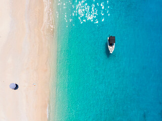 Aerial top down view to a secluded paradise beach on the island of Kefalonia with a moored boat over the clear, turquoise sea 