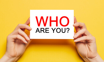 Female hands hold card paper with text Who are you on a yellow background. Business and finance concept