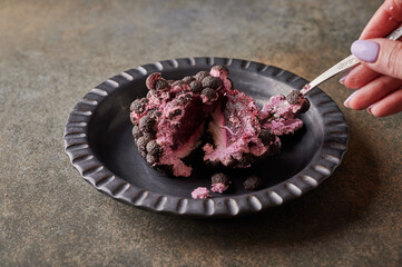 Woman's hand breaks with spoon original dessert fruit blackberry according to the idea of French confectioners - blackberry mousse, raspberry confit, mascarpone cream. Close up. Copy space