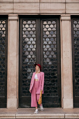 Street style, fashion conception: elegant woman wearing trendy pink suit, burgundy color hat, zebra print sneakers,  holding yellow bag, walking in street of city. Full-length outdoor portrait