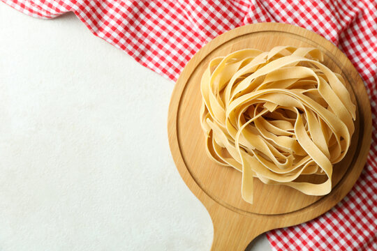 Board with uncooked pasta and kitchen towel on white textured background