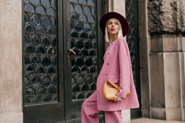 Street style, fashion conception: elegant woman wearing trendy pink suit, burgundy color hat,...