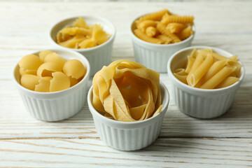 Bowls with uncooked pasta on white wooden background