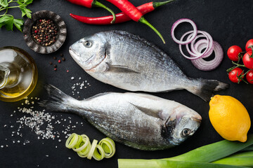 Fototapeta na wymiar Two uncooked dorado fishes on black background with spices and vegetables for cooking, top view