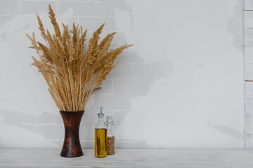 a vase of dried plants and bottles of oil against a light brick wall