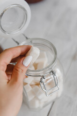 a close-up hand takes sugar cubes from a clear glass jar