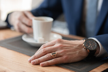 Fototapeta na wymiar a man in a suit and with a watch in his arms drinks coffee from a white glass