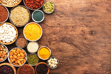 Superfoods, legumes, cereals, nuts, seeds set in bowls on wooden background. Superfood as chia, spirulina, beans, goji berries, quinoa, turmeric and other. Top view