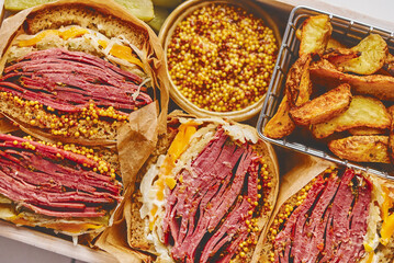 Enormous sandwiches with pastrami beef in wooden box. Served with baked potatoes, pickles
