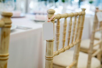 Empty nametag hanging on a side of the wooden vintage chair placed next to a dining table, l
little empty name card on chair of the guest