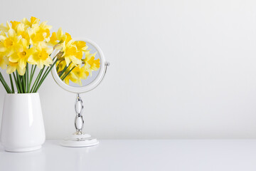 Daffodils in vase and reflection of yellow flowers in  mirror on white background