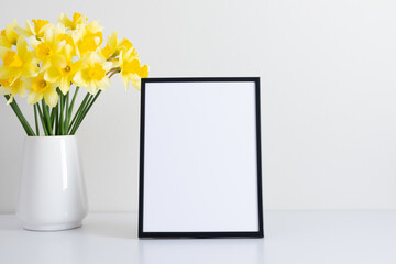 Yellow daffodils in vase, photo frame on white background.