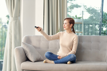Photo of happy young woman sitting on sofa at home. Looking camera holding remote control watch TV.