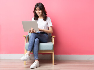 Asian woman sitting on sofa using laptop with happy expression