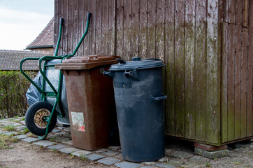 Naklejka premium Garbage cans and a wheelbarrow lean against a wooden shed