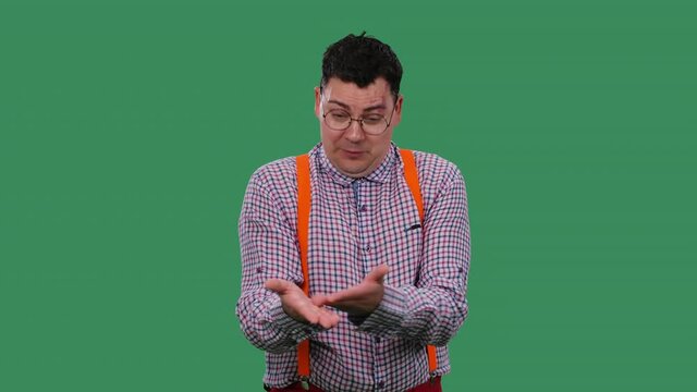 A portrait of a man who talks about something, points at something with his hands, justifies himself, shrugs his shoulders. A man in glasses in the studio on a green screen. Slow motion. Close up.