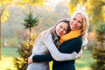 Fototapeta premium Portrait of a mother and daughter in nature, they are hugging, the girl put her head on her mother's shoulder and closed her eyes for joy, a happy joint moment
