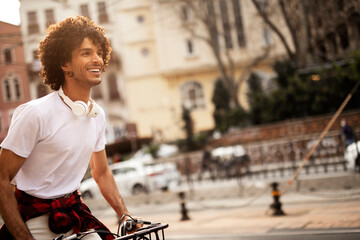 Happy young man riding bicycle in the city. Man with curly hair listening the music.