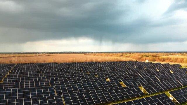 Aerial View Of Solar Panels Farm With Storm Clouds. Ecology Concept. Drone Flying Above Solar Panels Field Renewable Green Alternative Energy Concept. 