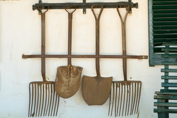 Fototapeta na wymiar rusted farm or agricultural implements or tools hanging on a wall as exterior decor feature