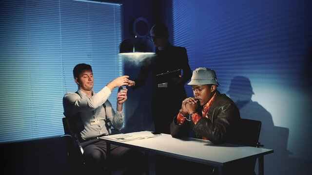 Caucasian detectives giving suspected black guy a glass of water in interrogation room