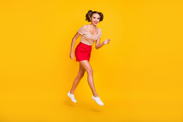 Fototapeta na wymiar Full length photo of girl with ponytails jump go wear striped t-shirt short skirt sneakers isolated yellow color background