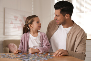 Fototapeta premium Man and his little daughter playing with puzzles at home