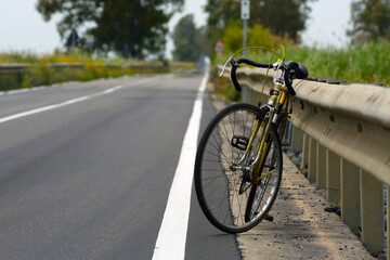 Bicicletta vintage da corsa abbandonata sul bordo di una strada dritta e lunga, appoggiata al...