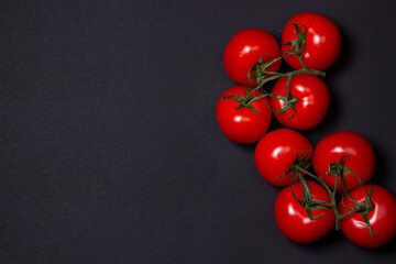 Tomatoes on a black background. Tomatoes on a vine on a dark background. Ripe fresh vegetables. © Ruzanna