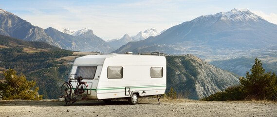 Caravan trailer, bicycle and car parked on a mountaintop with a view on French Alps near lake Lac de Serre-Poncon. Transportation, RV, motorhome, road trip, camping, tourism, recreation, lifestyle - obrazy, fototapety, plakaty