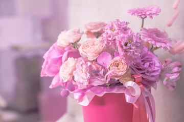 A lush bouquet of pink, purple, peach colour, white cute delicate small roses of different sizes, flowers in cylindrical bright box vase.