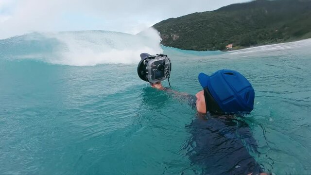 Surf photographer. Man with camera in underwater housing takes picture of the breaking wave
