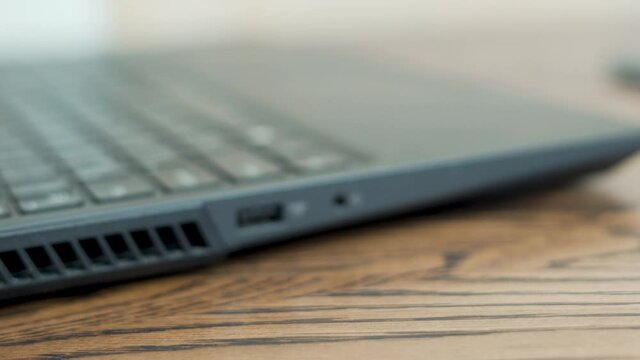 Close-up of A Hand Sticking Out A Flash Drive Memory Card from the USB Port of a Laptop on a Wooden Table. Hand, Memory Card, Flash Drive, Laptop, Closeup.