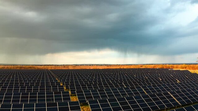 Flying above Solar Power Station Panels in the fields. Storm rain clouds in background. Aerial drone view of Green energy Plant