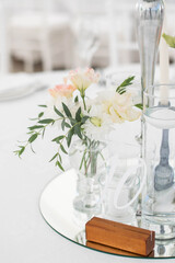 Close-up of a wedding dinner table at reception. Fresh flowers and candles on mirros plate. Wedding decorations.